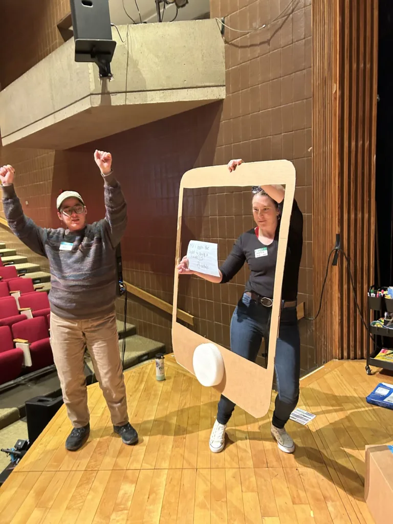 person dancing and person holding large cardboard frame replica of smart phone