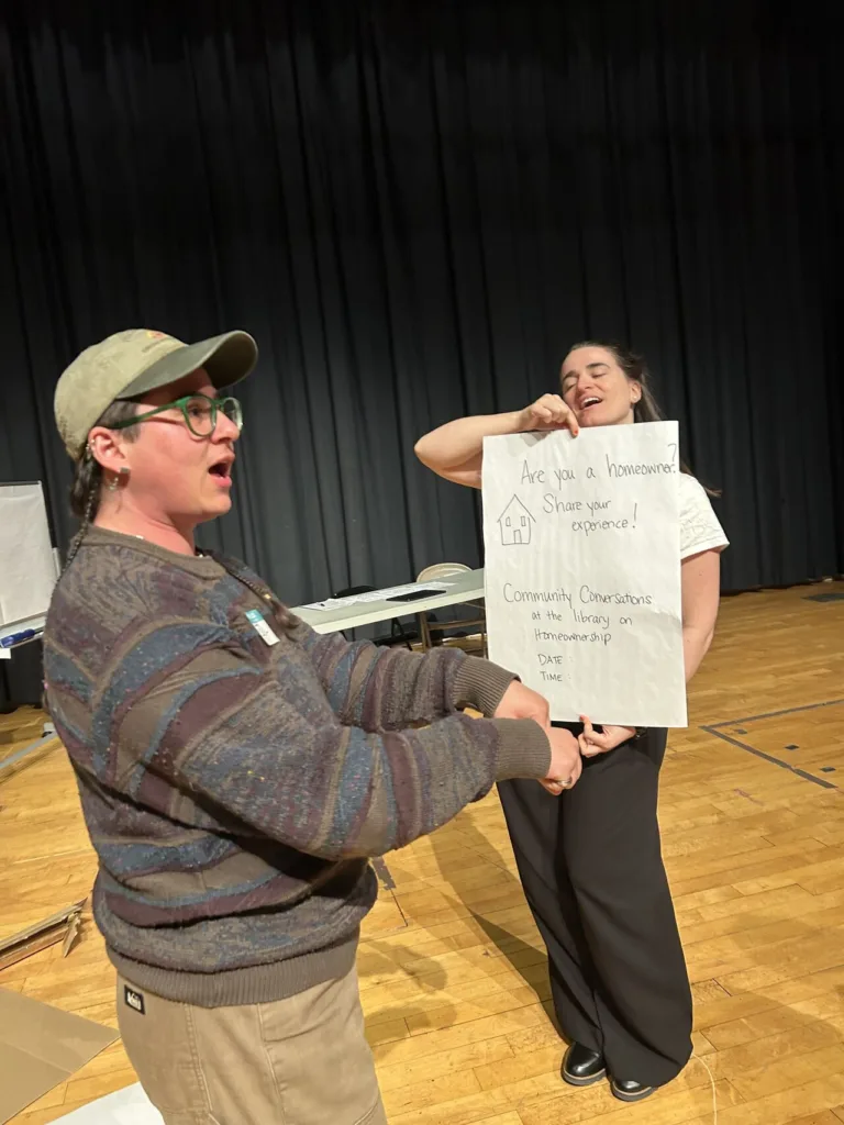 person holding a large poster and person pantomiming pushing a shopping cart